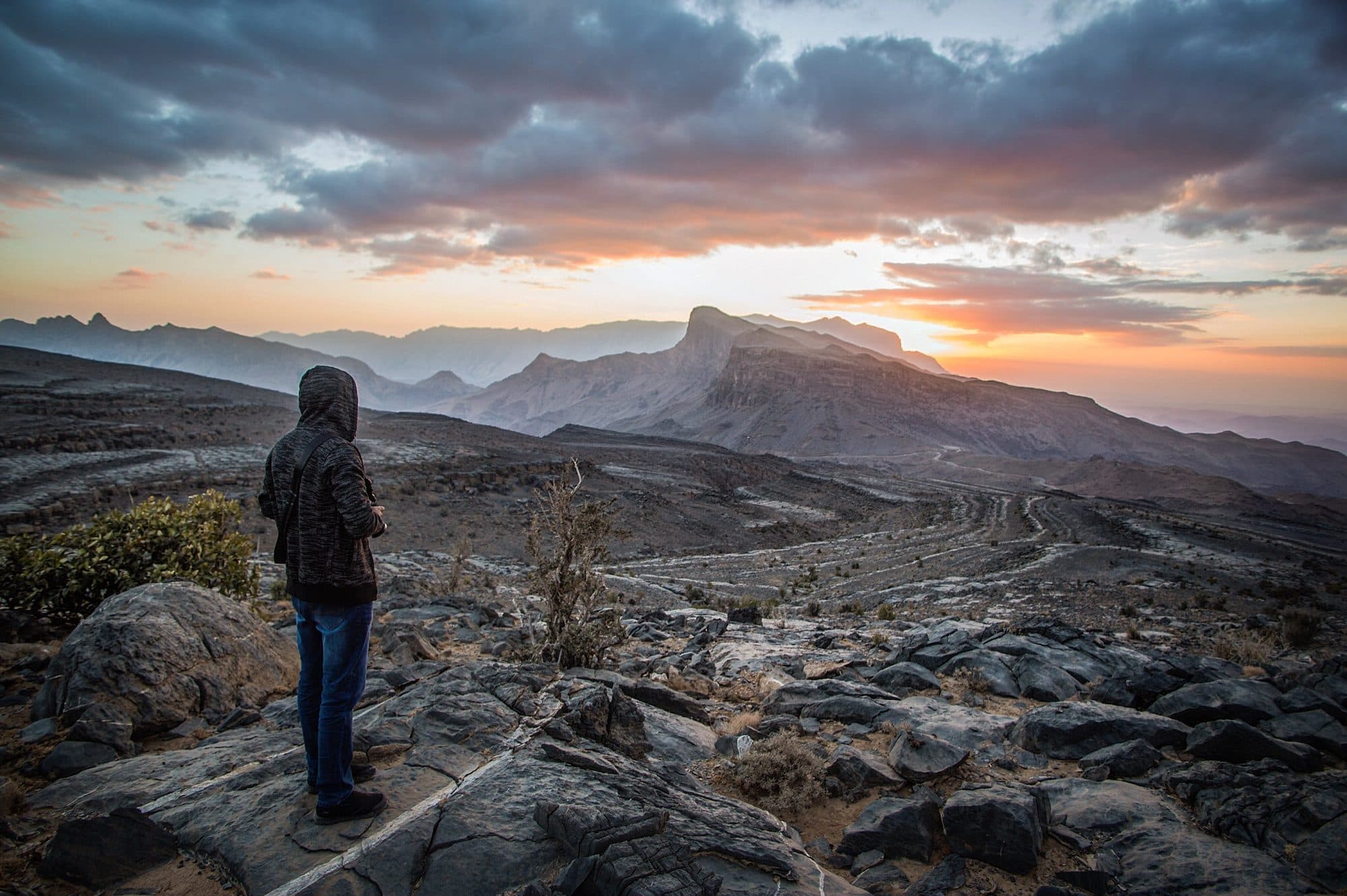 A hiker on the rocky rim of Jebel Shams under a dramatic evening sky
